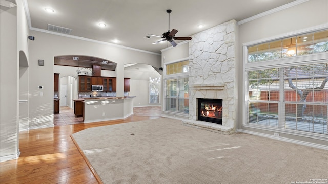 living room featuring hardwood / wood-style flooring, ceiling fan, a stone fireplace, and crown molding