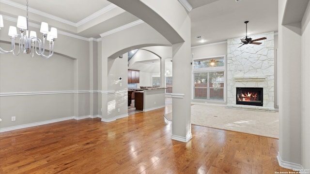 unfurnished living room featuring ceiling fan with notable chandelier, a fireplace, light wood-type flooring, and ornamental molding