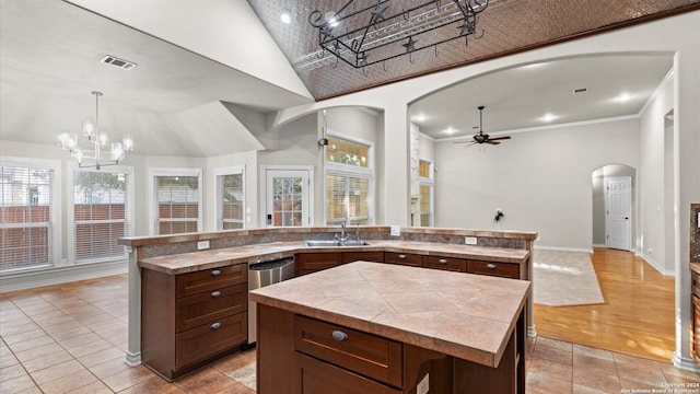 kitchen with a wealth of natural light, ceiling fan with notable chandelier, a kitchen island with sink, and sink