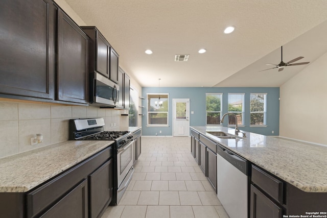 kitchen with sink, stainless steel appliances, decorative backsplash, a center island with sink, and ceiling fan with notable chandelier