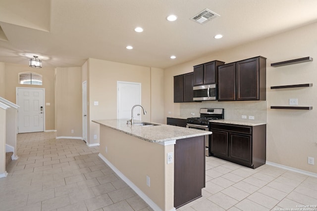 kitchen featuring a center island with sink, sink, light stone countertops, dark brown cabinetry, and stainless steel appliances