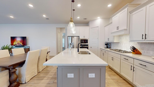 kitchen with appliances with stainless steel finishes, sink, decorative light fixtures, light hardwood / wood-style floors, and an island with sink