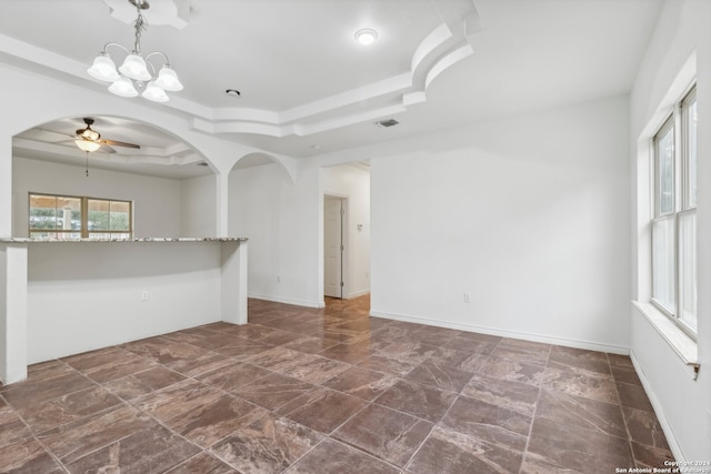 spare room featuring a raised ceiling and ceiling fan with notable chandelier