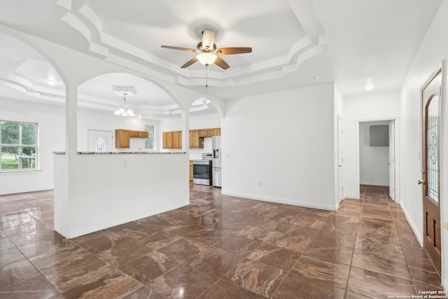 unfurnished living room with a tray ceiling and ceiling fan with notable chandelier