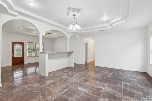 unfurnished room featuring ceiling fan with notable chandelier and a raised ceiling