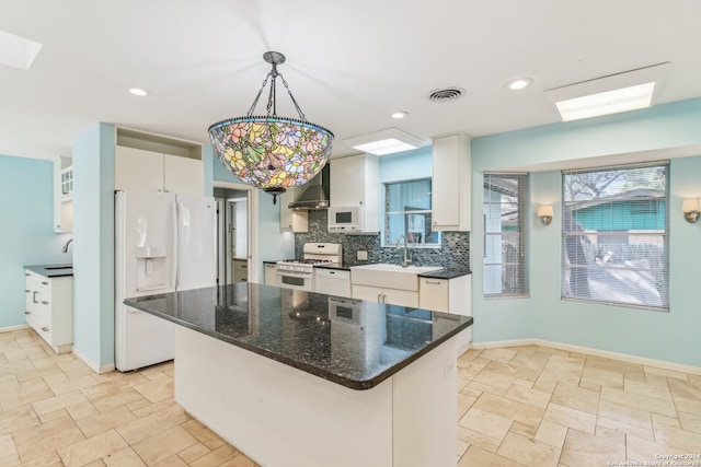 kitchen featuring pendant lighting, white appliances, wall chimney exhaust hood, a kitchen island, and white cabinetry