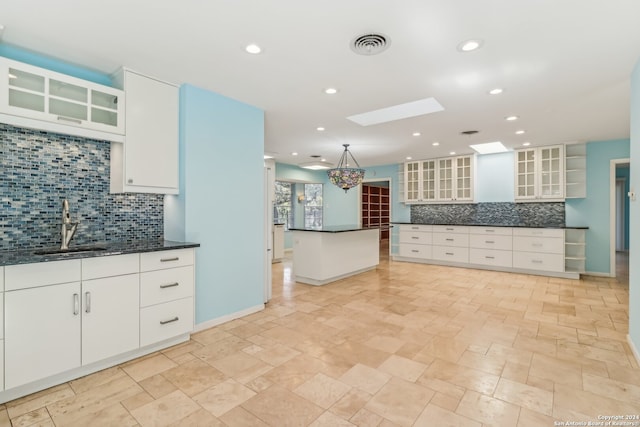 kitchen featuring decorative backsplash, white cabinetry, sink, and a skylight