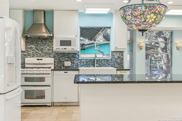 kitchen with sink, wall chimney range hood, dark stone countertops, white appliances, and white cabinets