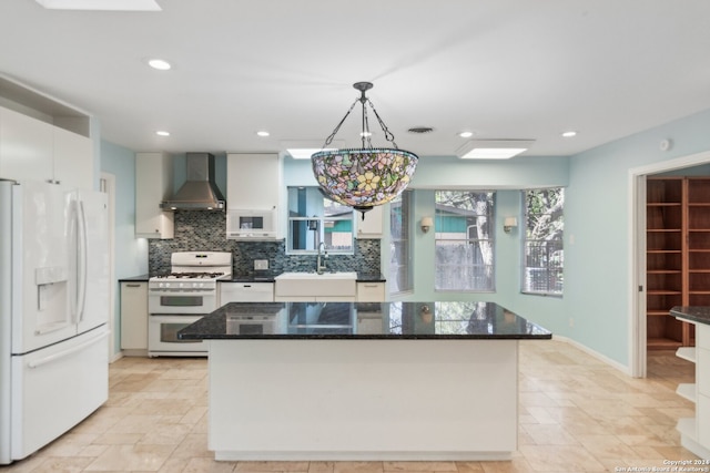 kitchen with white appliances, wall chimney range hood, sink, hanging light fixtures, and a kitchen island