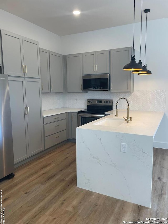 kitchen with kitchen peninsula, appliances with stainless steel finishes, dark hardwood / wood-style flooring, decorative light fixtures, and gray cabinets