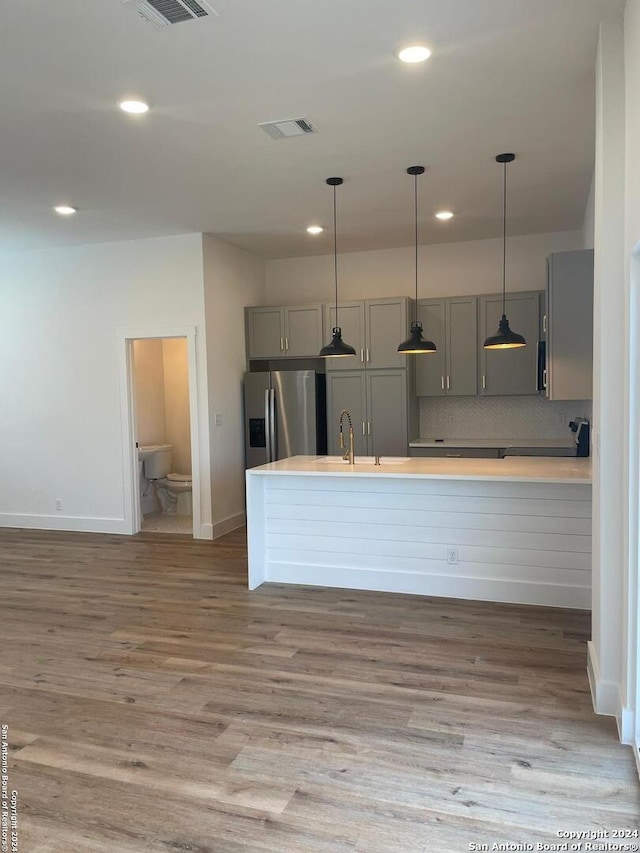 kitchen featuring sink, stainless steel refrigerator with ice dispenser, pendant lighting, gray cabinets, and hardwood / wood-style flooring