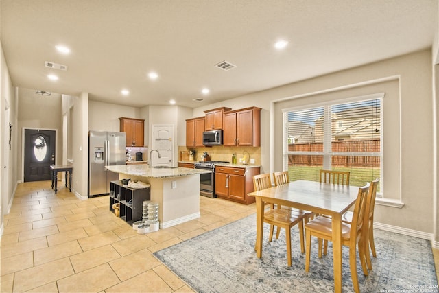 kitchen with light stone countertops, sink, backsplash, a kitchen island with sink, and appliances with stainless steel finishes