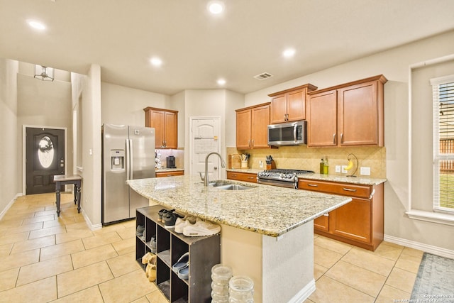 kitchen featuring appliances with stainless steel finishes, tasteful backsplash, sink, light tile patterned floors, and an island with sink