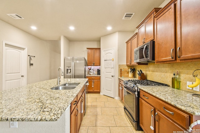 kitchen with a center island with sink, sink, light stone countertops, appliances with stainless steel finishes, and tasteful backsplash