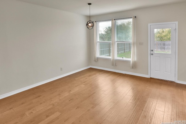 unfurnished dining area featuring an inviting chandelier, a wealth of natural light, and light hardwood / wood-style floors