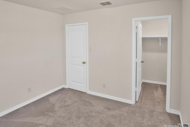 unfurnished bedroom featuring a walk in closet, light colored carpet, and a closet