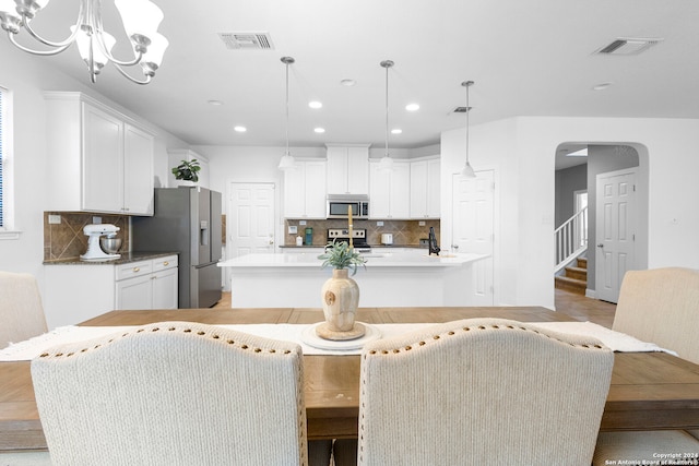 kitchen with decorative backsplash, white cabinetry, hanging light fixtures, and appliances with stainless steel finishes