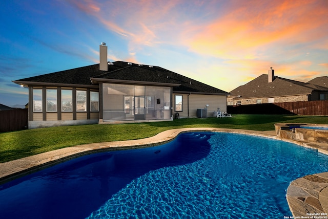 pool at dusk featuring a sunroom, a yard, an in ground hot tub, and central AC