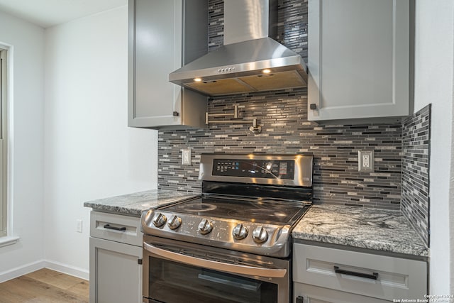 kitchen featuring light stone countertops, light hardwood / wood-style flooring, wall chimney exhaust hood, and stainless steel electric range