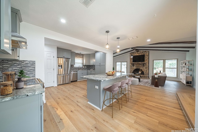 kitchen with hanging light fixtures, light hardwood / wood-style flooring, lofted ceiling with beams, a fireplace, and appliances with stainless steel finishes