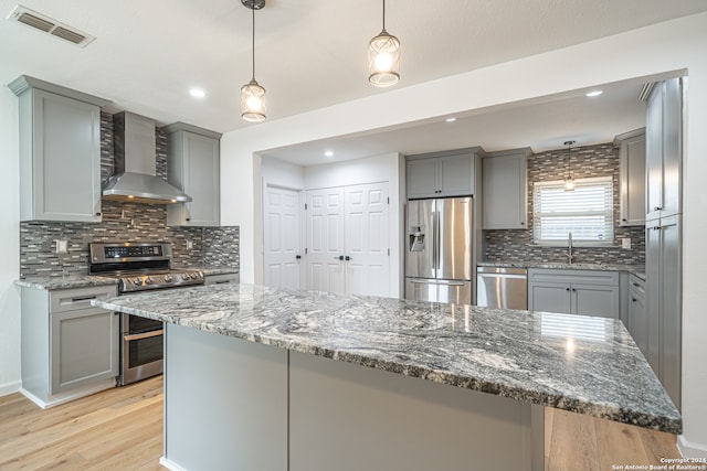 kitchen with decorative backsplash, appliances with stainless steel finishes, dark stone counters, wall chimney exhaust hood, and light hardwood / wood-style floors