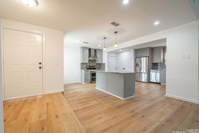 kitchen with wall chimney exhaust hood, stainless steel appliances, pendant lighting, a center island, and gray cabinets