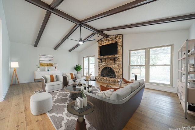 living room with light wood-type flooring, lofted ceiling with beams, a stone fireplace, and ceiling fan