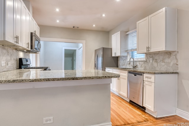 kitchen with kitchen peninsula, appliances with stainless steel finishes, light wood-type flooring, light stone counters, and white cabinetry