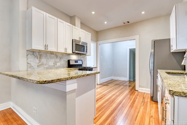 kitchen with light hardwood / wood-style floors, white cabinetry, kitchen peninsula, and appliances with stainless steel finishes