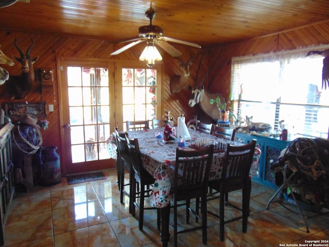 tiled dining room featuring wooden walls, ceiling fan, and wooden ceiling