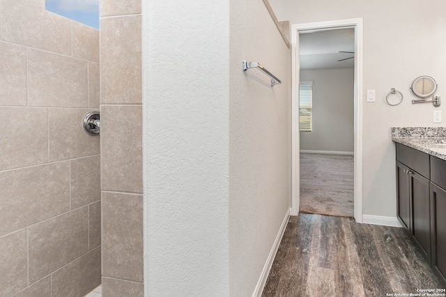 bathroom with a tile shower, plenty of natural light, vanity, and wood-type flooring