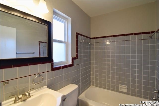 full bathroom with tiled shower / bath, vanity, toilet, and tile walls