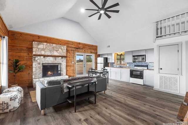 living room featuring ceiling fan, a stone fireplace, dark hardwood / wood-style flooring, high vaulted ceiling, and wood walls