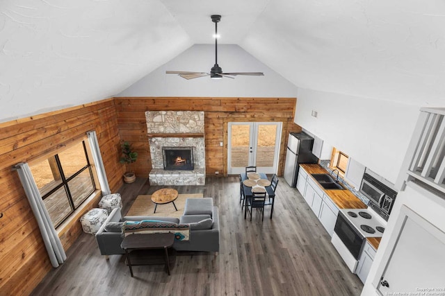 living room with dark hardwood / wood-style flooring, a stone fireplace, and wooden walls