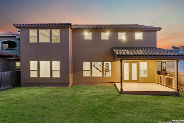 back house at dusk featuring a patio and a lawn