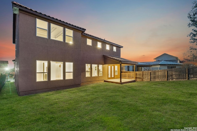 back house at dusk featuring a lawn