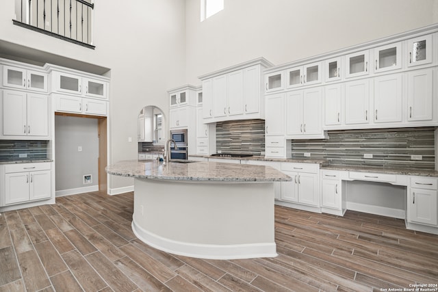 kitchen with stainless steel appliances, white cabinets, light stone counters, an island with sink, and a high ceiling