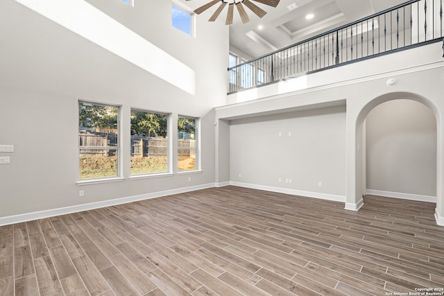 unfurnished living room featuring a towering ceiling, wood-type flooring, and ceiling fan