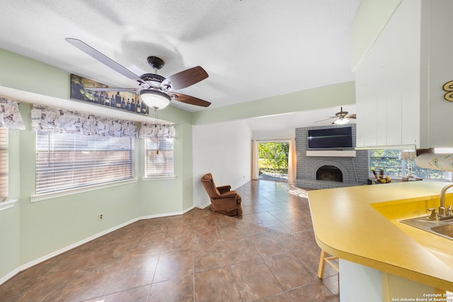 interior space with a textured ceiling, ceiling fan, sink, and a fireplace