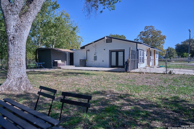 back of house featuring a lawn, central air condition unit, french doors, an outdoor structure, and a patio