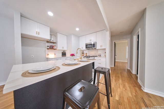 kitchen featuring tasteful backsplash, a kitchen breakfast bar, light hardwood / wood-style floors, a center island with sink, and white cabinets