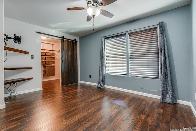 unfurnished bedroom featuring a barn door, dark hardwood / wood-style floors, and ceiling fan