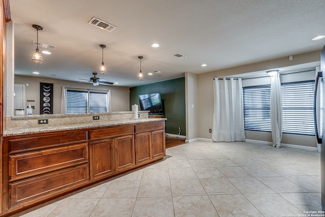 kitchen featuring pendant lighting, ceiling fan, light tile patterned flooring, and light stone countertops