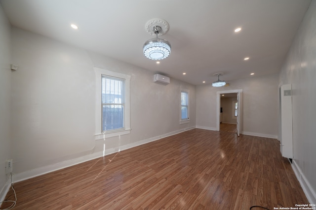 empty room featuring a chandelier, a wall unit AC, plenty of natural light, and dark wood-type flooring