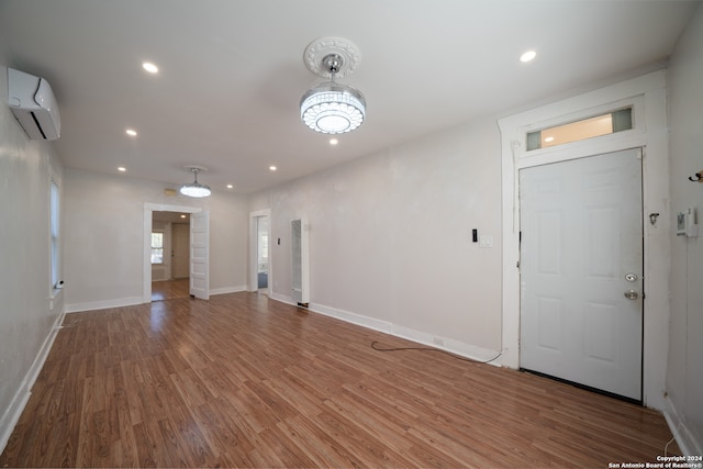 entrance foyer featuring hardwood / wood-style flooring, a wall mounted AC, and a notable chandelier