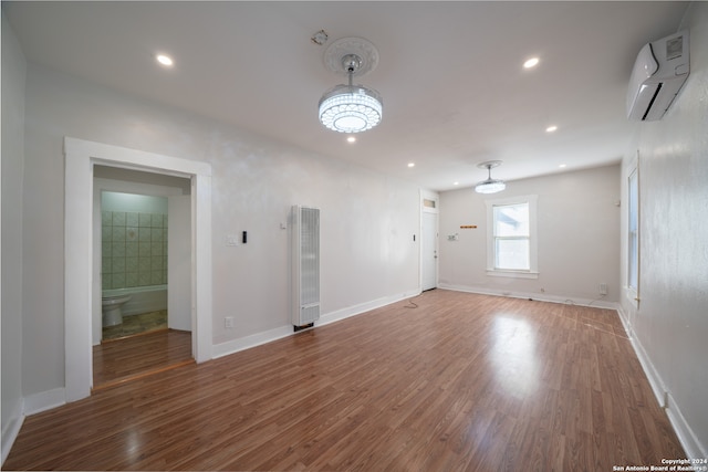 spare room featuring a wall unit AC, dark hardwood / wood-style flooring, and a notable chandelier