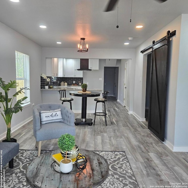 living room featuring ceiling fan with notable chandelier, a barn door, and light hardwood / wood-style floors