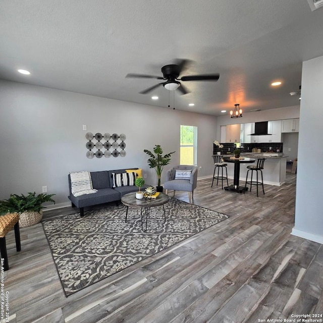 living room with ceiling fan with notable chandelier, wood-type flooring, and a textured ceiling