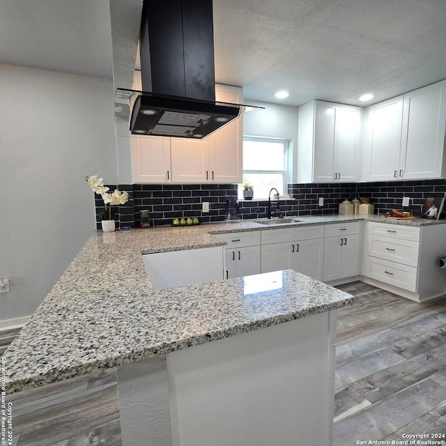 kitchen with kitchen peninsula, white cabinetry, sink, and island exhaust hood