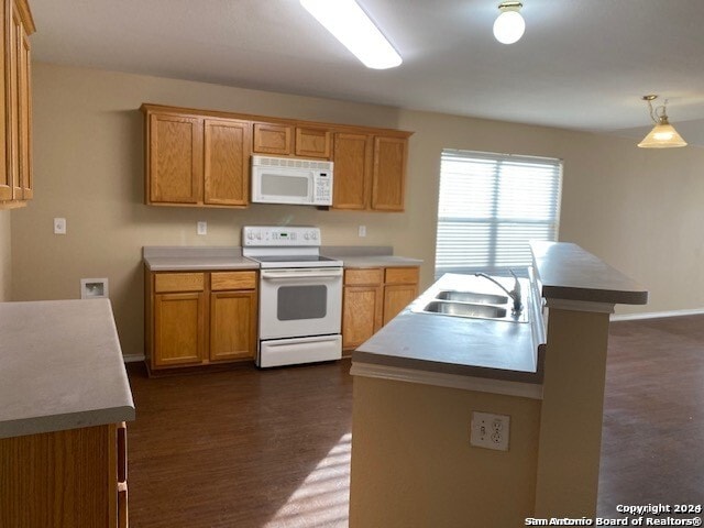 kitchen with sink, dark wood-type flooring, hanging light fixtures, white appliances, and a kitchen island with sink